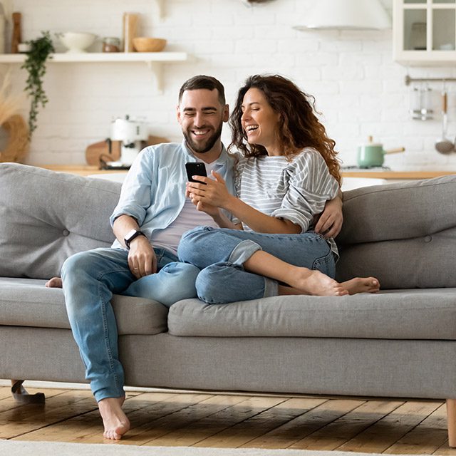 Happy young couple on couch looking at mobile